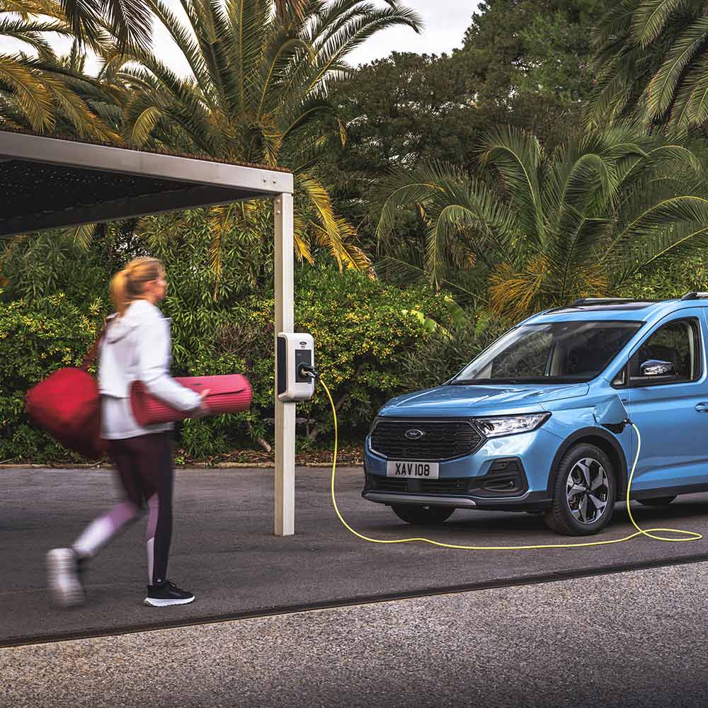 Uma pessoa com um tapete de ioga caminhando em direção a uma van híbrida plug-in Ford Tourneo Connect.