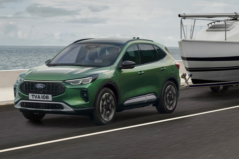 Ford Kuga verde a rebocar um pequeno barco ao longo de uma estrada costeira.