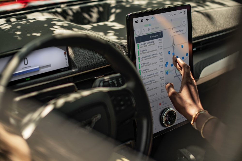 Grande plano de uma mulher num Ford Mustang Mach-E a interagir com o grande ecrã táctil do SYNC.