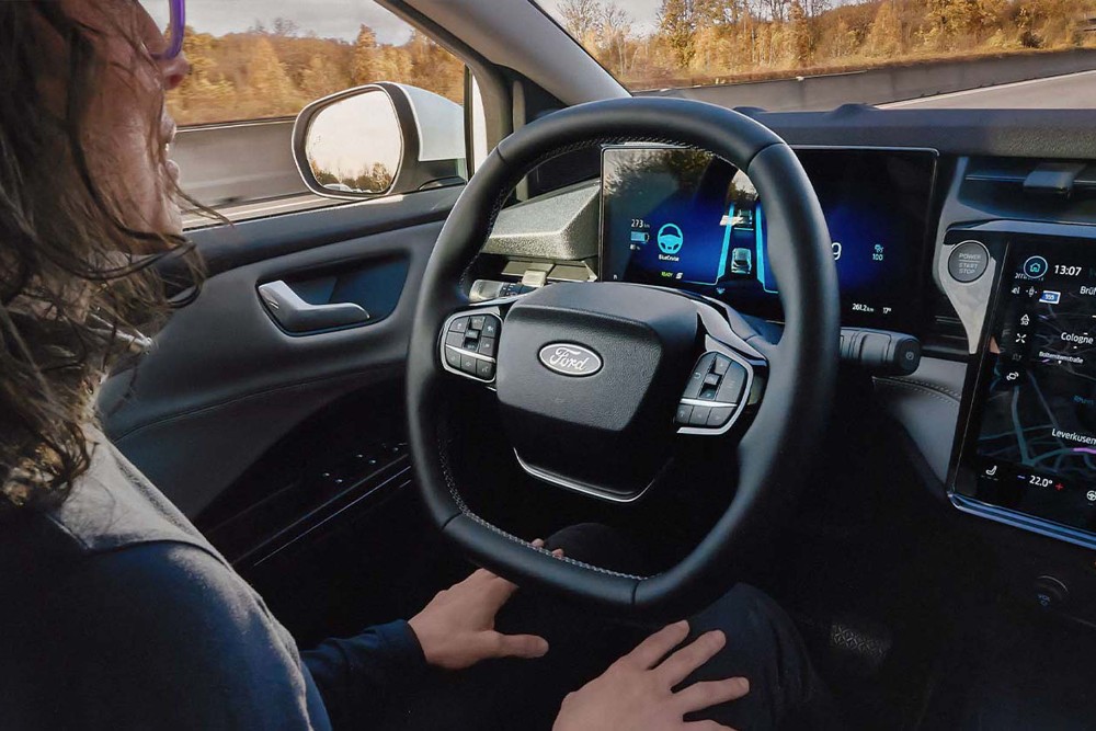 Vista desde o interior, de uma mulher a conduzir um Ford Puma equipado com BlueCruise, com as mãos fora do volante.