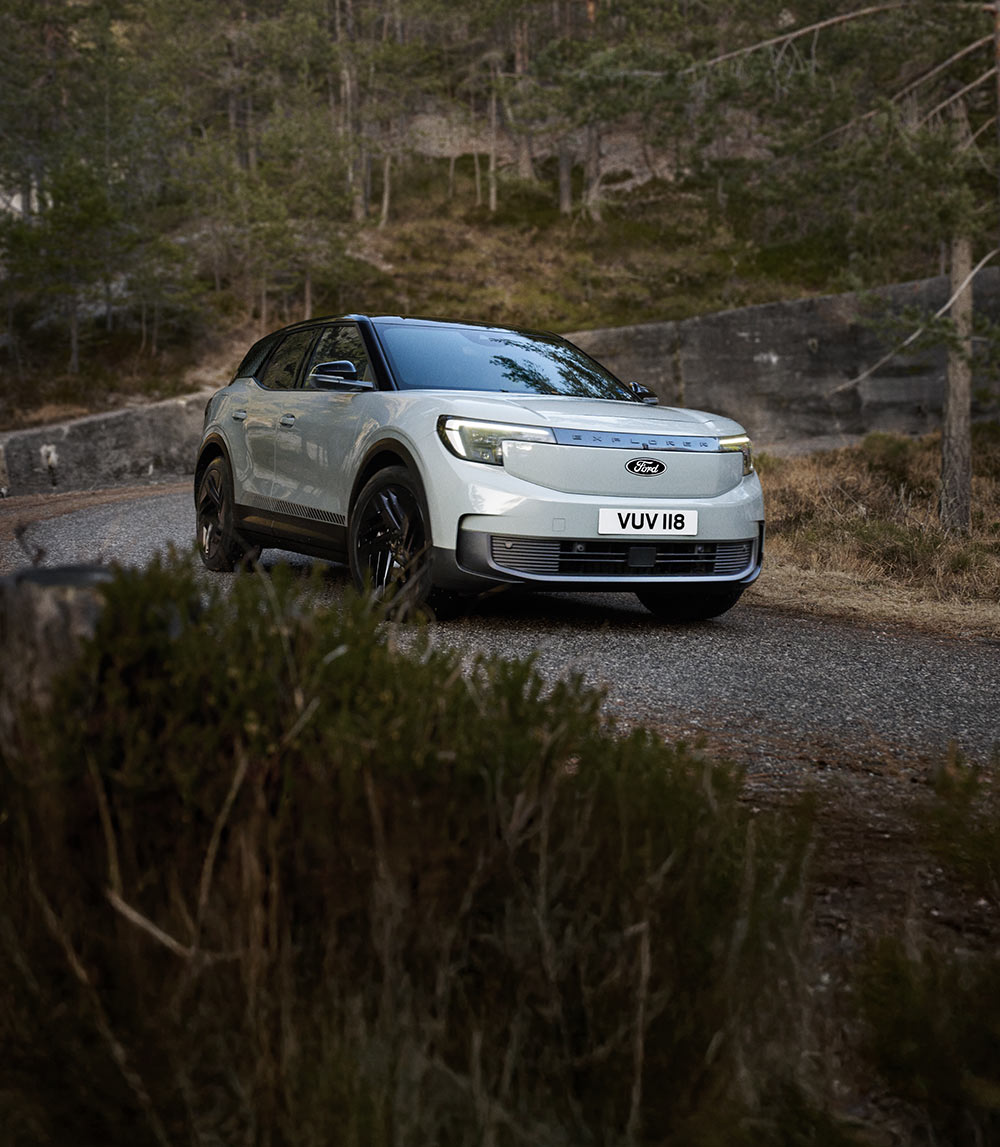 Ford Explorer prateado a percorrer uma estrada montanhosa sinuosa. 