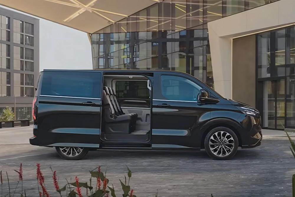 Ford E-Tourneo Custom preto estacionado com a porta lateral aberta, a revelar os bancos interiores.