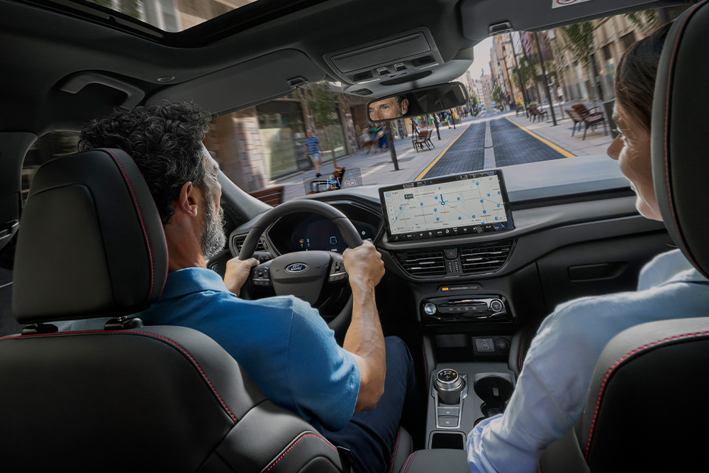 Duas pessoas num Ford Kuga a conduzir numa rua da cidade a usar as instruções do ecrã digital de 12,3