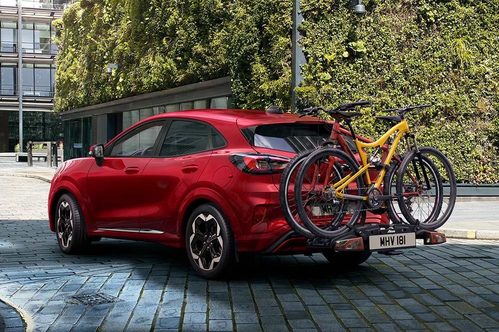 Ford Puma vermelho estacionado num ambiente urbano com duas bicicletas montadas num suporte traseiro para bicicletas.