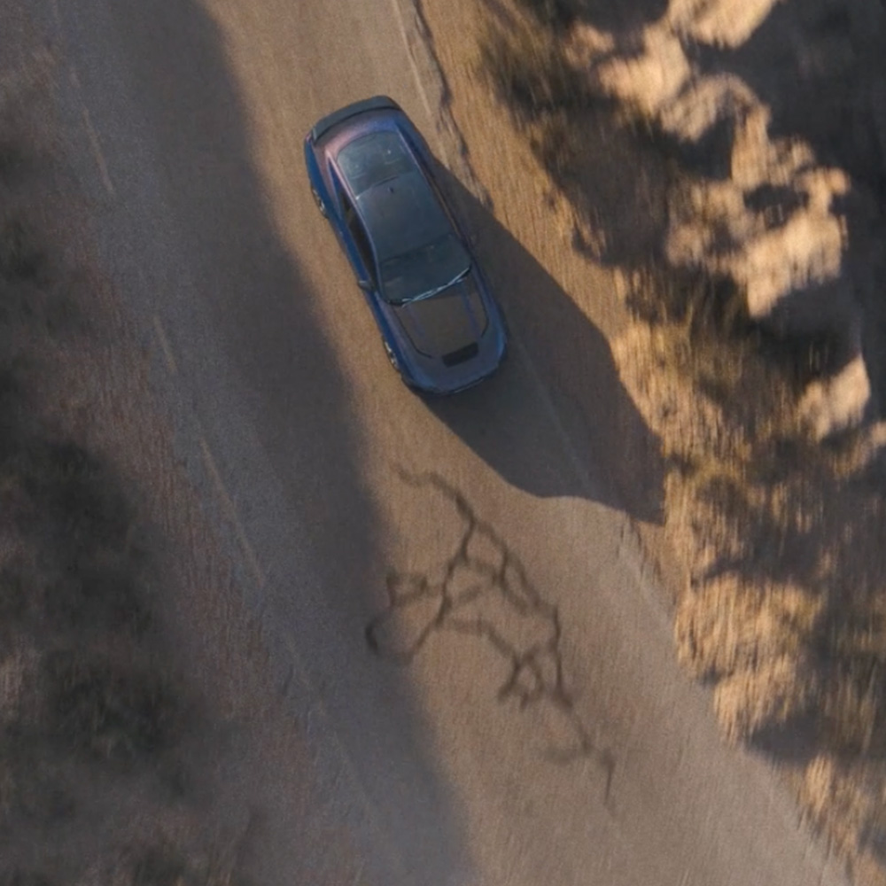 Uma fotografia aérea de um Ford Mustang Dark Horse Fastback com pintura Blue Ember a conduzir ao longo de uma estrada de montanha.