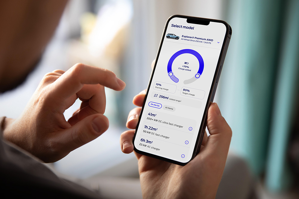 Uma pessoa segurando um smartphone com o aplicativo Ford exibindo uma interface de progresso de carregamento de veículo elétrico.