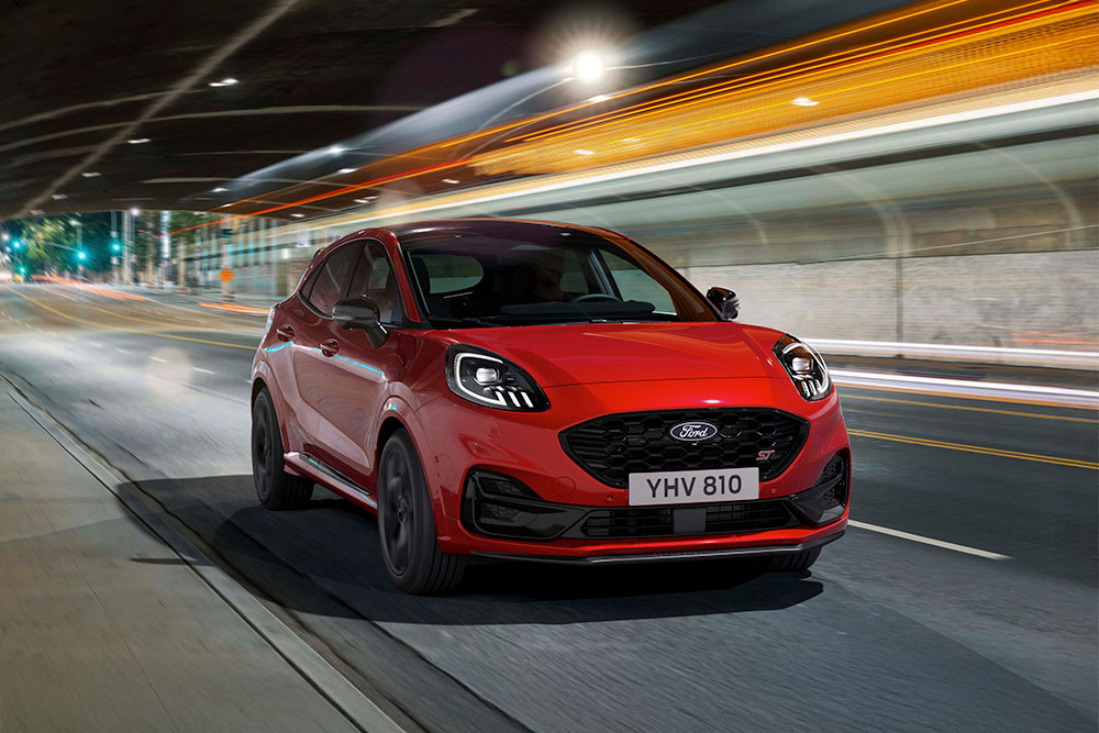 Um SUV desportivo vermelho Ford Puma ST a percorrer uma estrada iluminada da cidade à noite.