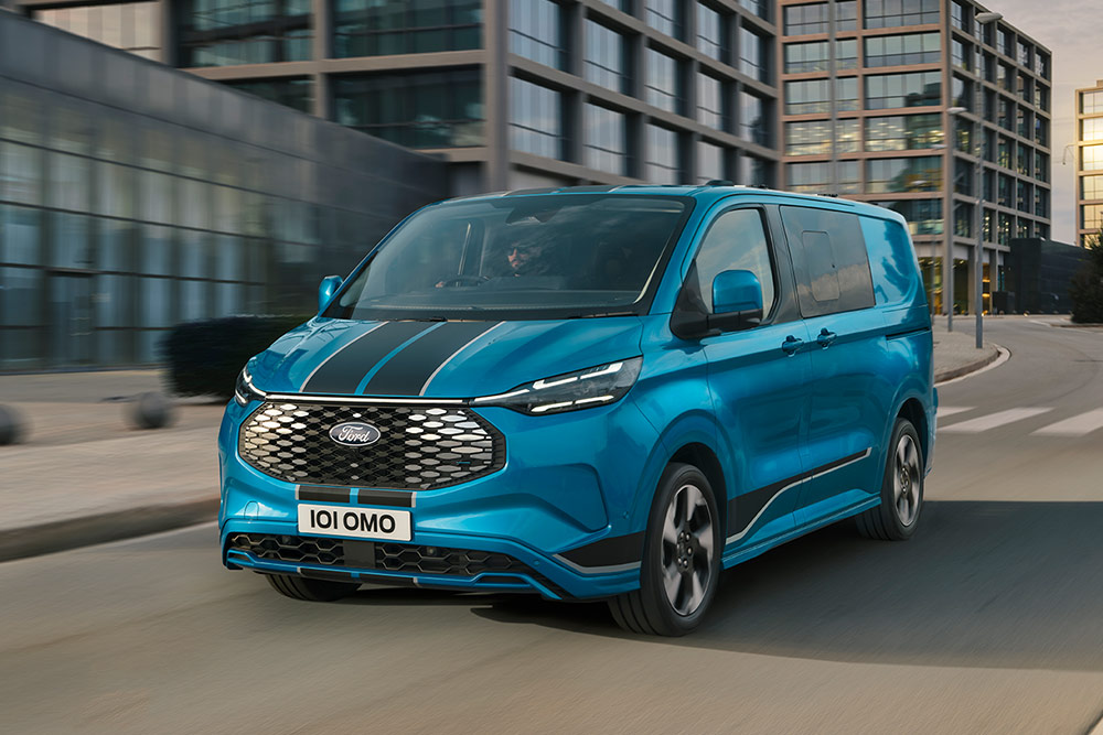 Ford E-Transit Custom Sport de cabina dupla azul a circular numa rua urbana.