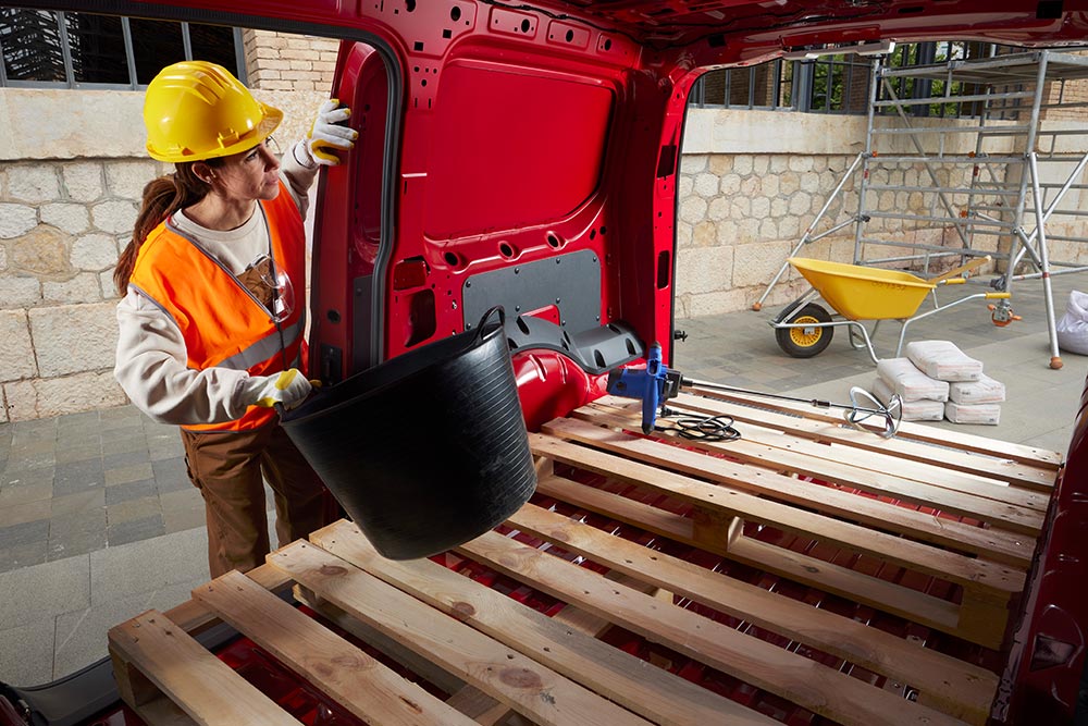 Mulher a colocar materiais de construção no espaço de carga de um Ford Transit Connect, com as portas laterais e traseiras abertas.