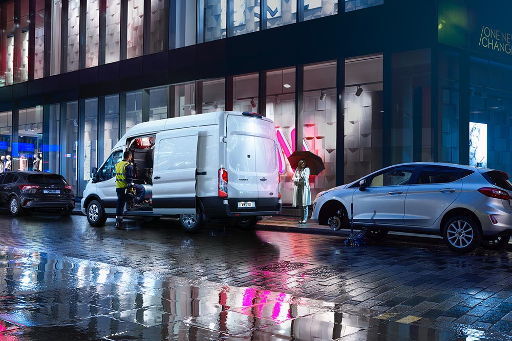 Carrinha Ford Transit de reboque estacionada numa cidade à noite.