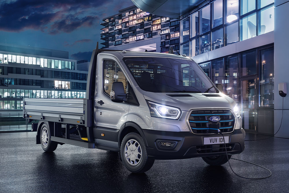 Ford E-Transit Chassis Cabina prateada estacionada em frente a um edifício moderno, de noite.