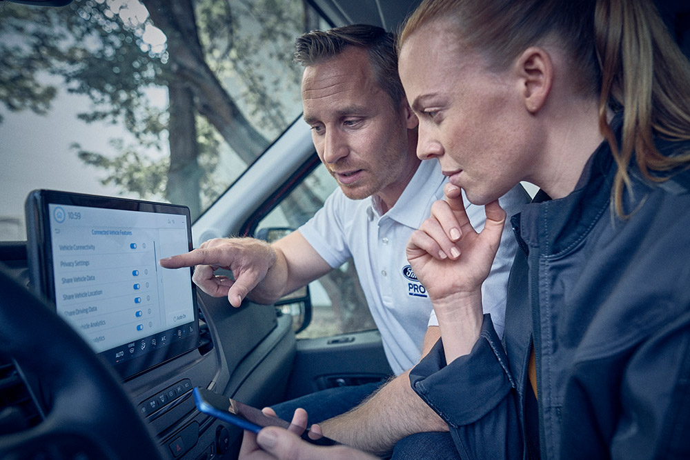 A Ford Pro uptime expert discussing fleet data with a customer, displayed on the digital screen of a Ford Transit van.