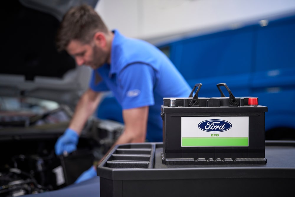 Mecânico Ford a trabalhar num motor de carro, com uma bateria de carro Ford em primeiro plano.